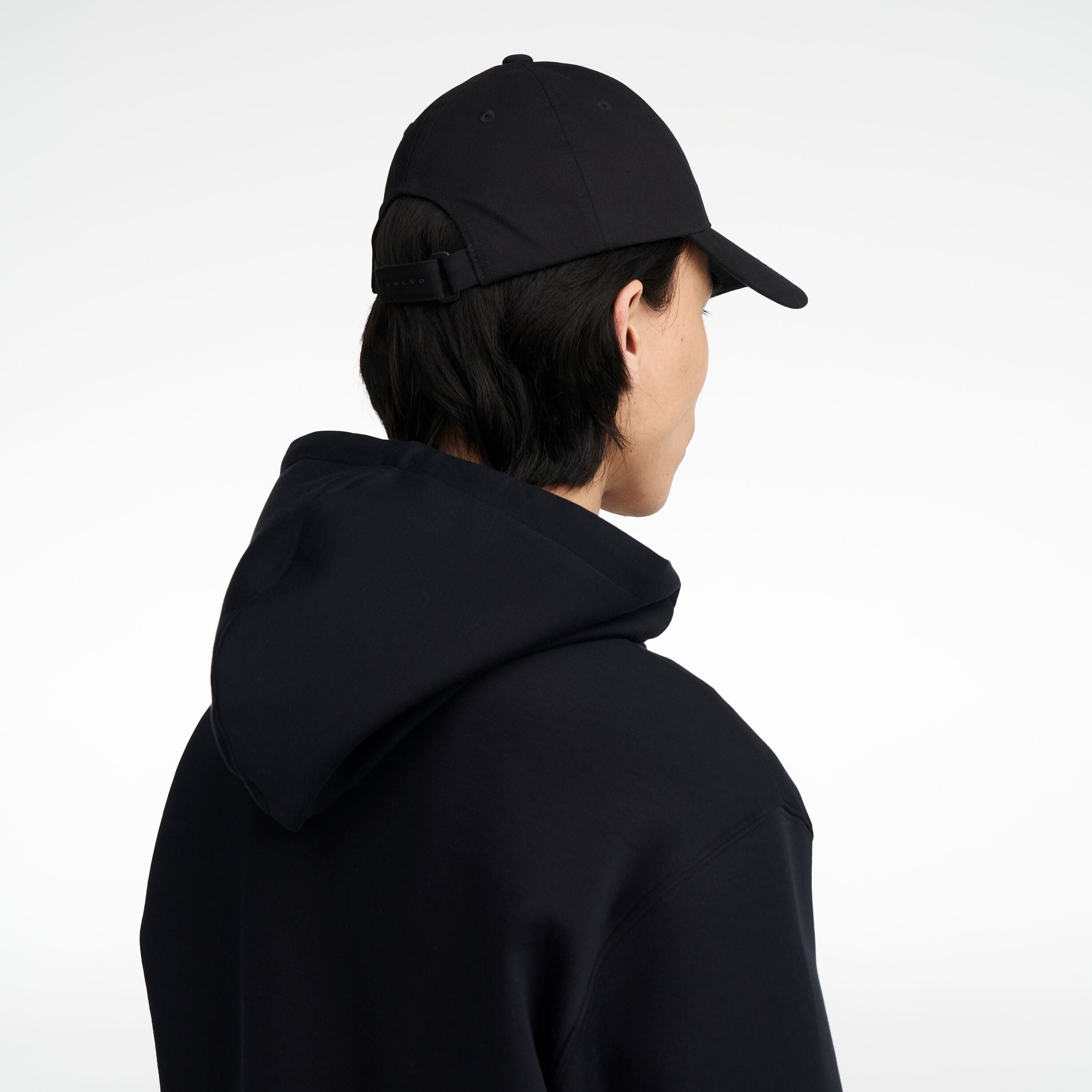 The Volvo Classic Cap in black, worn by a male model. It features an embroidered diagonal logo on the side. 