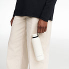Detailed shot of a male model carrying the Volvo Thermos Bottle, in off-white against a white background. We see the rust-proof stainless steel design with watertight seal at top.