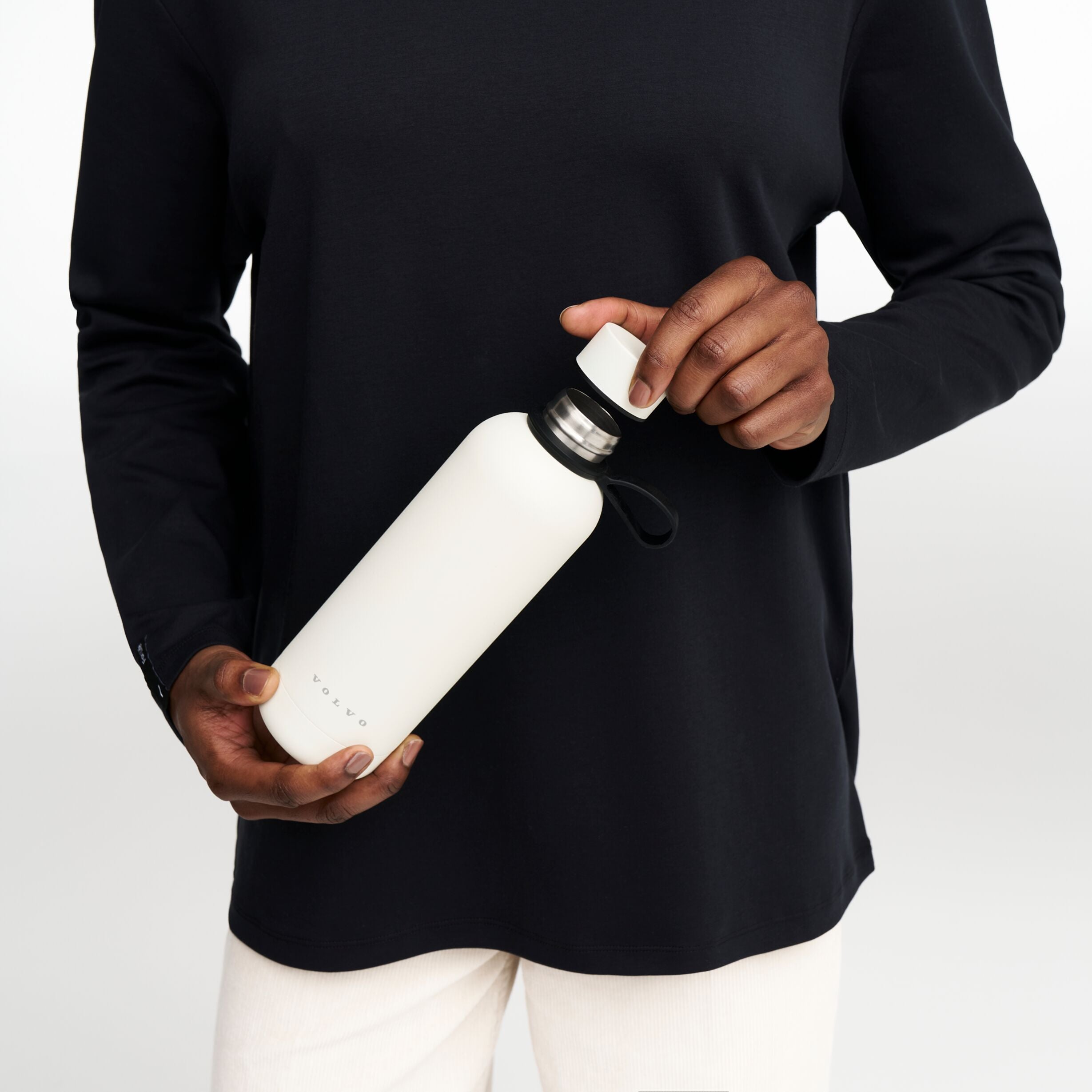 Detailed shot of a male model carrying the Volvo Thermos Bottle, in off-white against a white background. We see the rust-proof stainless steel design with watertight seal at top.