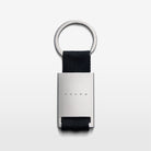The Volvo Key Chain in black against a white background. We see the solid metal with Volvo logo at the centre, with strap and key ring at the top.