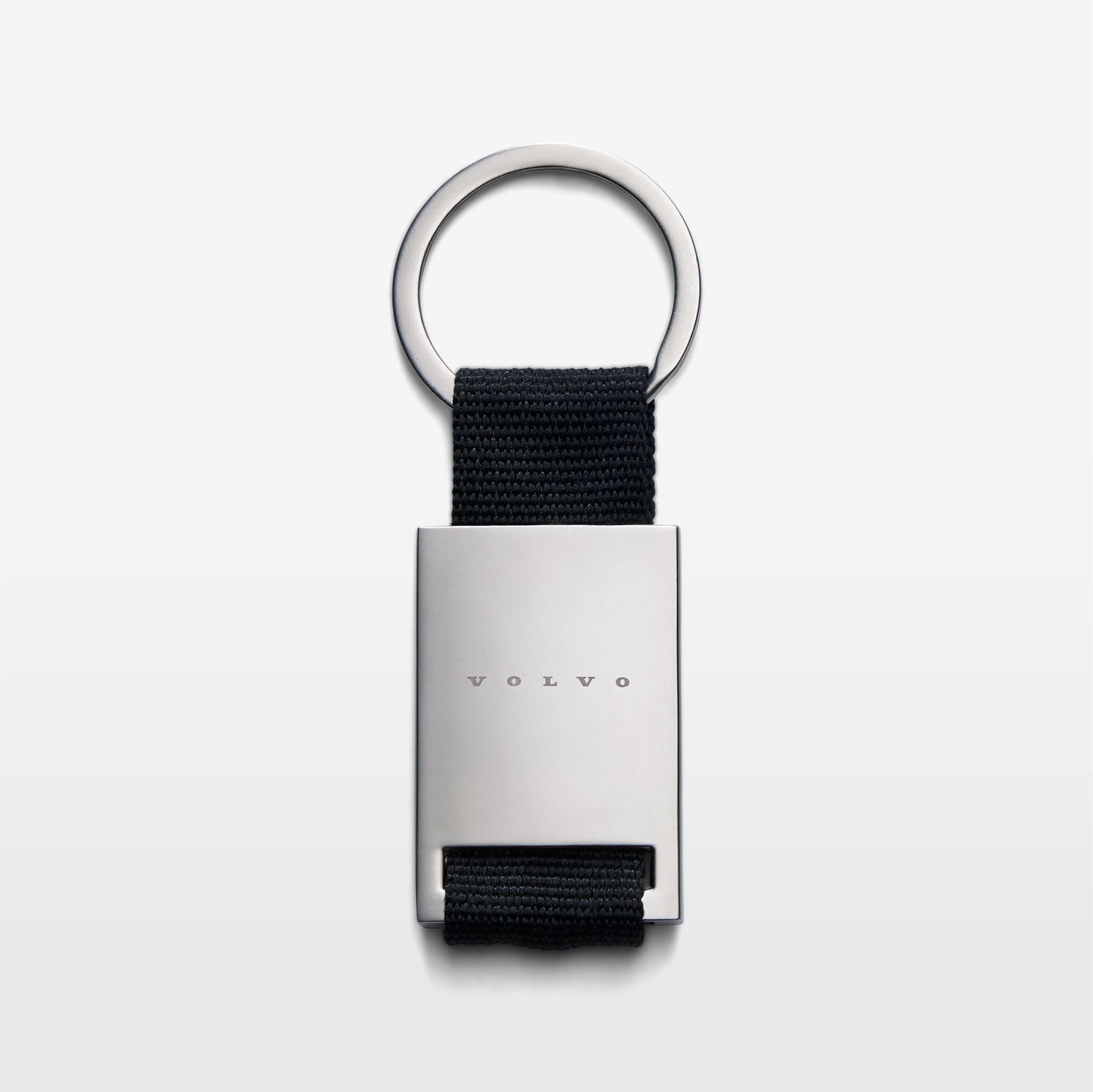 The Volvo Key Chain in black against a white background. We see the solid metal with Volvo logo at the centre, with strap and key ring at the top.