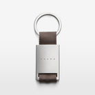 The Volvo Key Chain in grey against a white background. We see the solid metal with Volvo logo at the centre, with strap and key ring at the top.