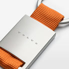 A close-up view of the Volvo Key Chain in orange.  We see the solid metal with Volvo logo at the centre, with strap and key ring at the top.