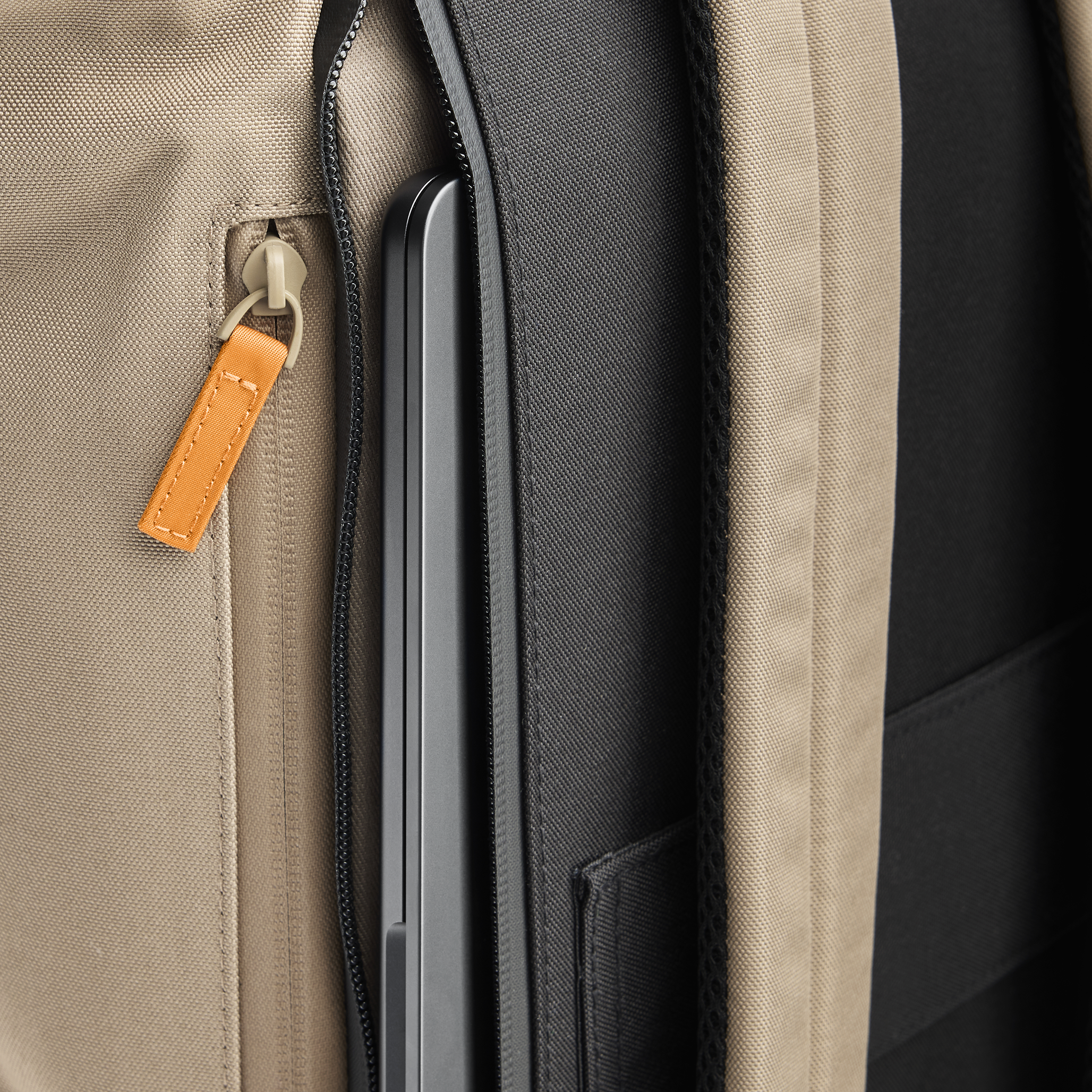 Detail view of Volvo Backpack from back left side. We see the unzipped reinforced pocket for easy laptop storage and orange puller on other practical storage pocket. The adjustable straps are visible.