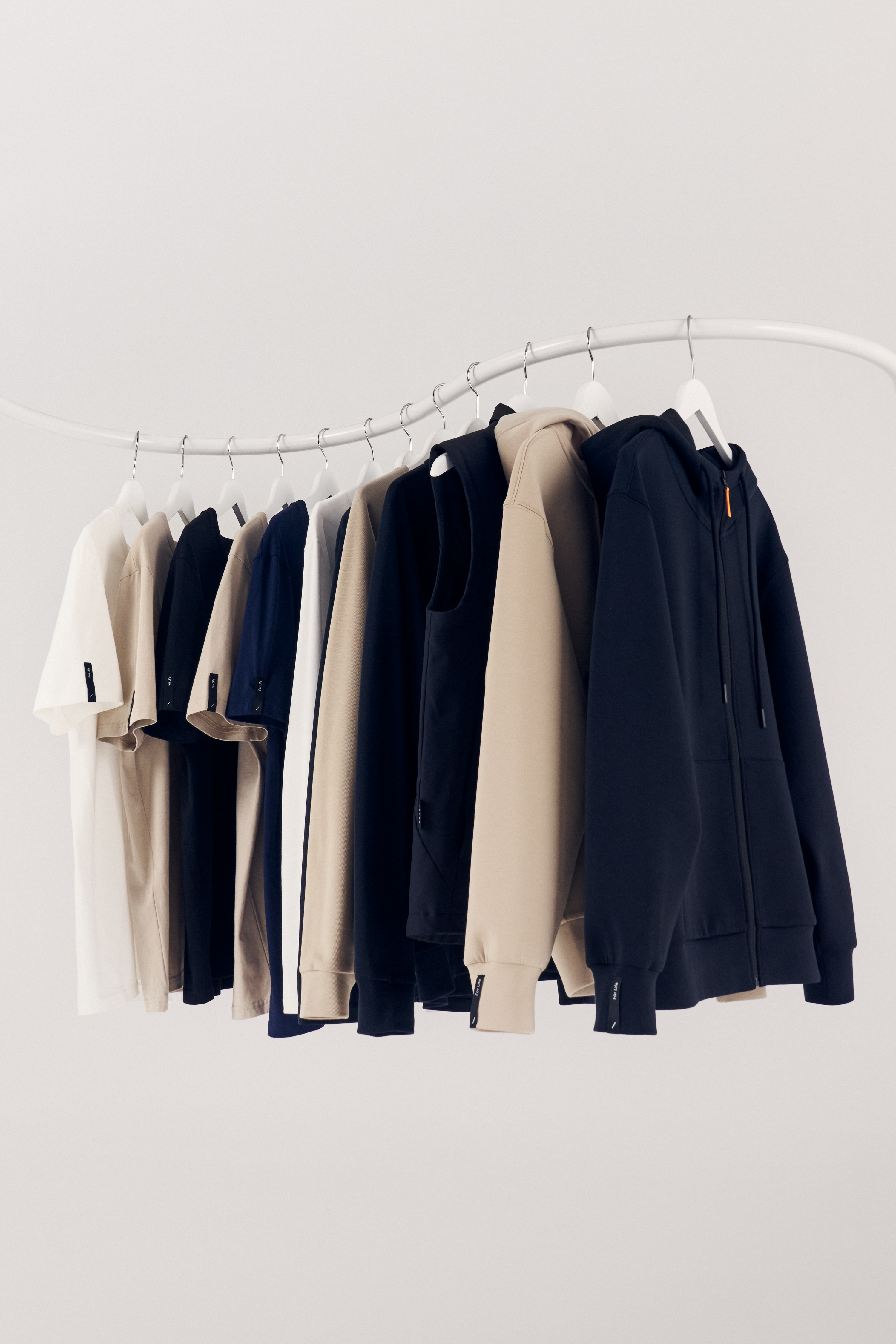 The Volvo clothing collection hanging on a rail against a light grey background. We see t-shirts, long sleeve t-shirts, sweatshirts, a vest jacket and zipped hoodies.
